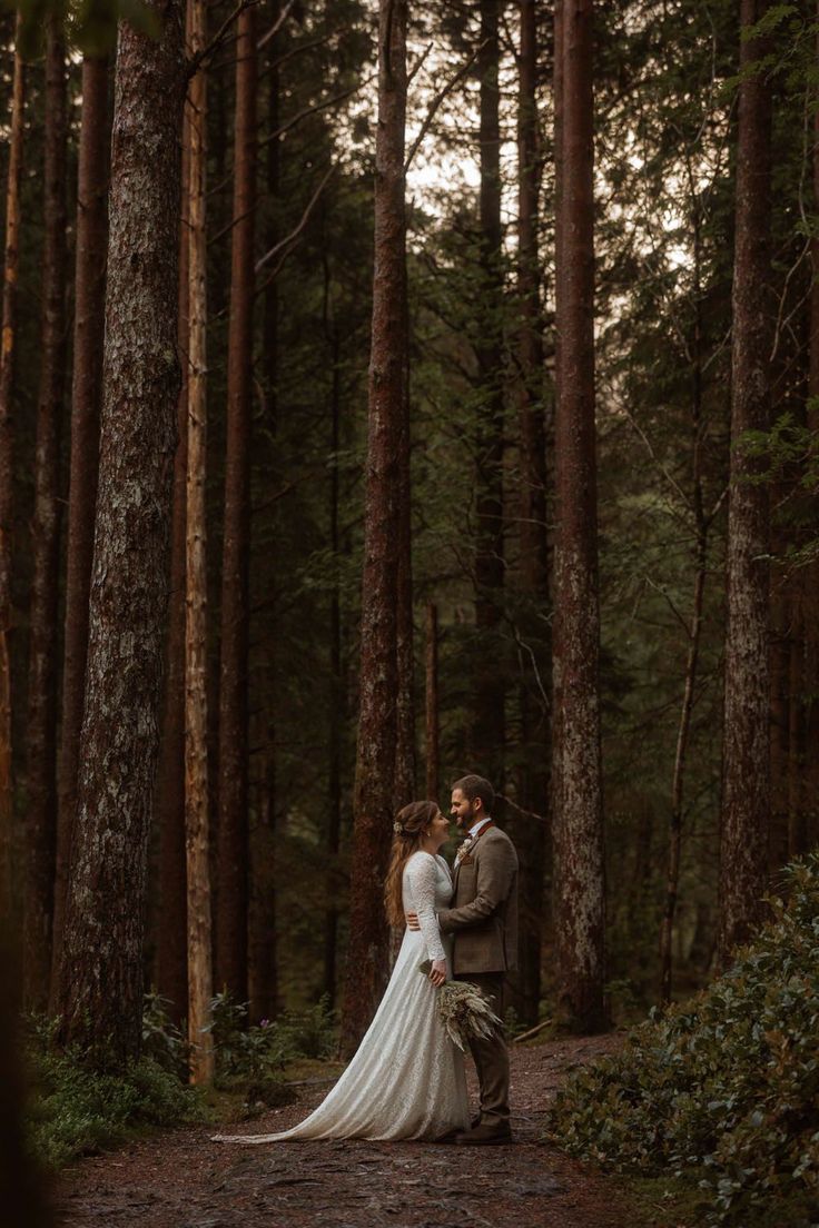 a bride and groom standing in the middle of a forest with tall trees behind them