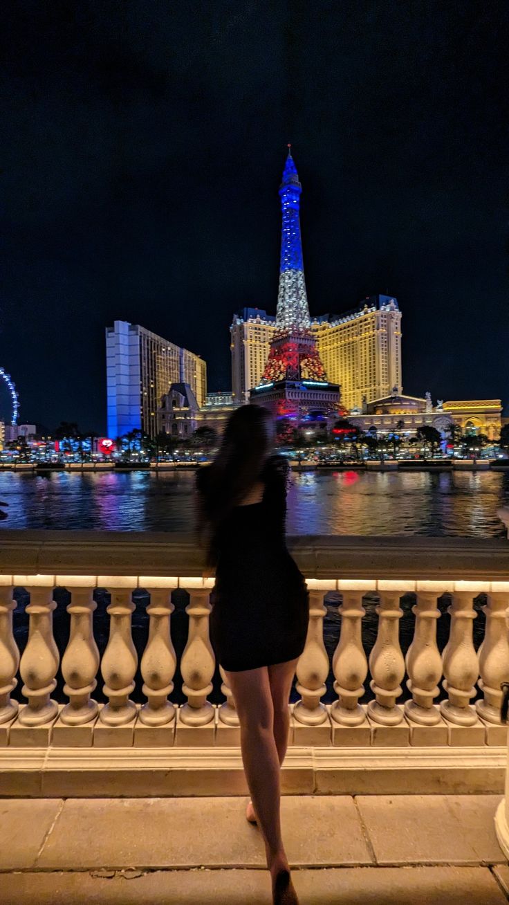 a woman standing next to a railing looking at the water and buildings in the background