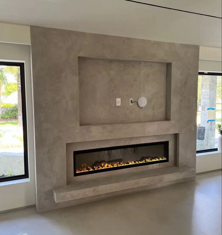 an empty living room with a fireplace in the center and large windows on both sides