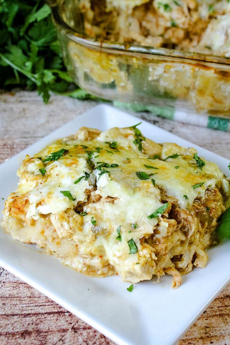 a square white plate topped with lasagna covered in cheese and herbs next to a casserole dish