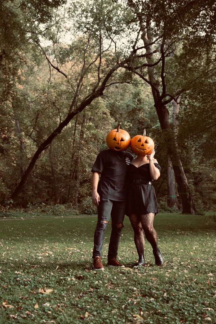 two people standing in the grass with pumpkins on their heads