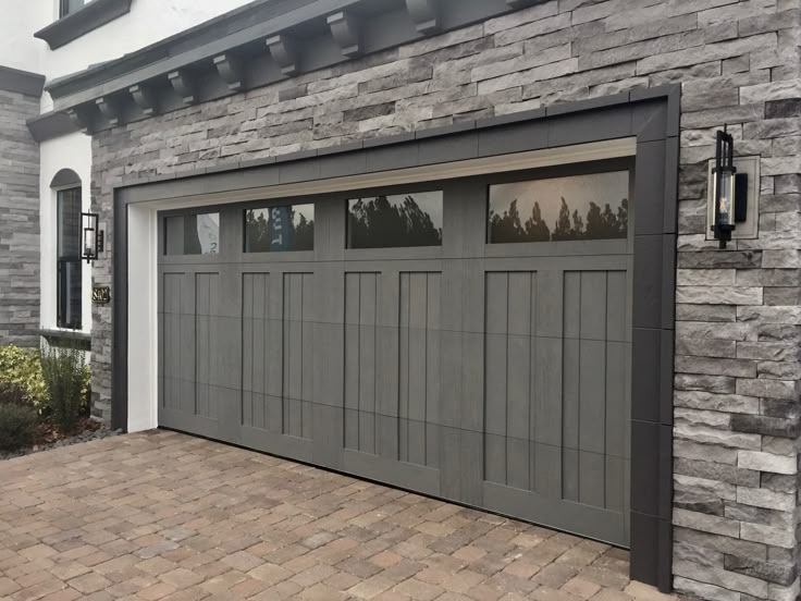 a gray garage door with windows on the side and brick walkway in front of it