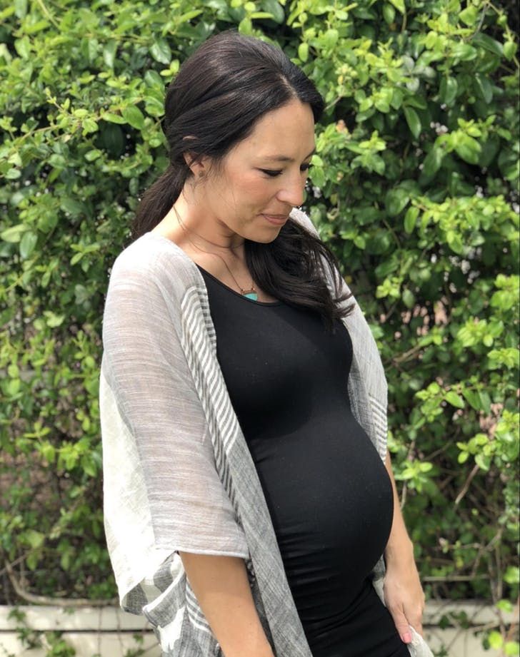 the pregnant woman is wearing a black dress and gray cardigan sweater, while she has her hand on her belly