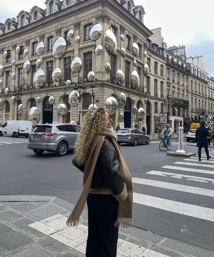 a woman is standing on the sidewalk in front of an old building with many mirrors