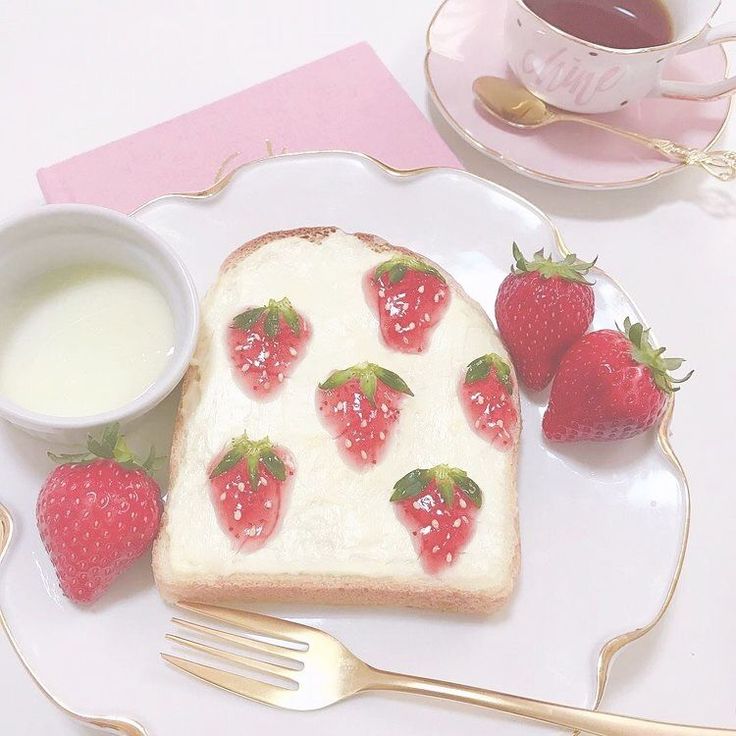 a piece of bread with strawberries on it next to a cup of milk and two forks