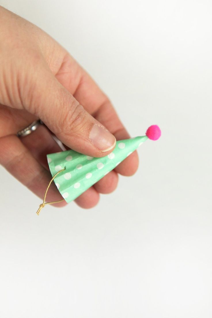 a hand holding a small green paper christmas tree ornament with pink pom - poms