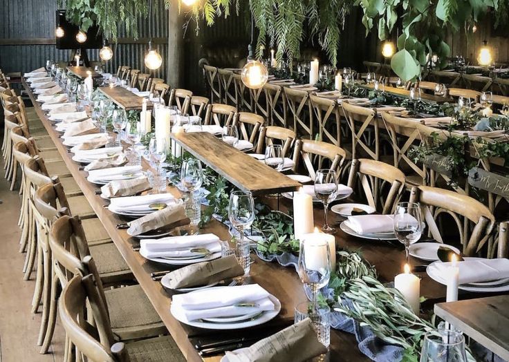 a long table set with place settings and candles in the center, surrounded by greenery