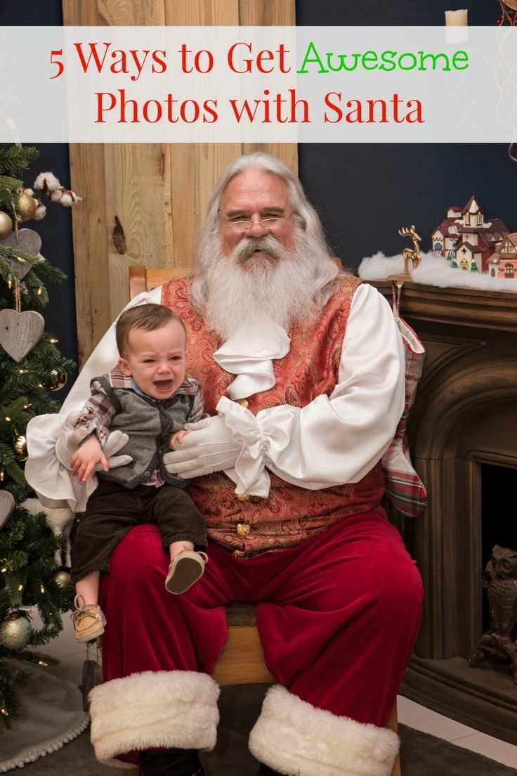 a man sitting next to a baby in front of a christmas tree with a santa clause on it