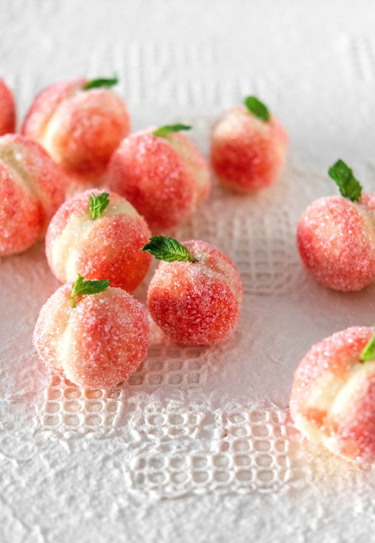 some sugar coated fruit sitting on top of a white doily with green leafy sprigs