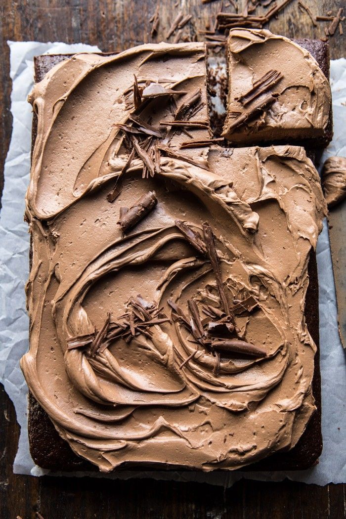 a chocolate cake with frosting on top sitting on a piece of paper next to a knife