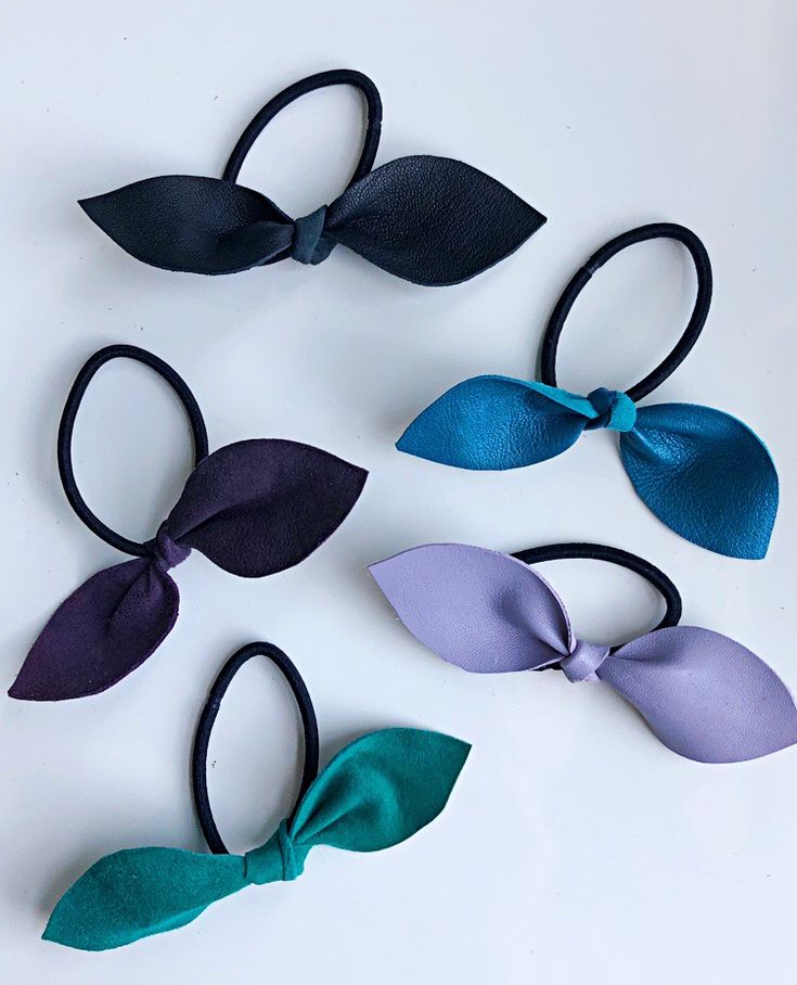 four different colors of hair bows on a white surface with one being blue, the other is purple and green