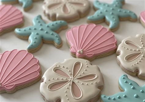 decorated cookies with shells and starfishs on a white tablecloth covered in blue, pink and gray icing