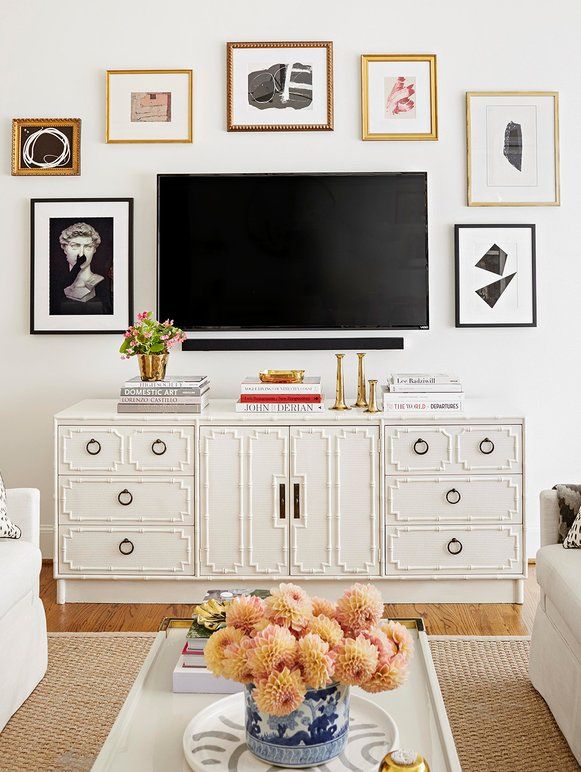 a living room with white furniture and pictures on the wall above it's tv