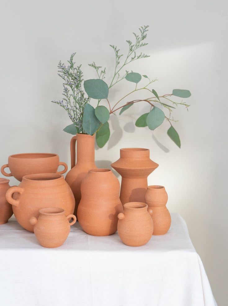 a group of clay vases sitting on top of a table next to a plant