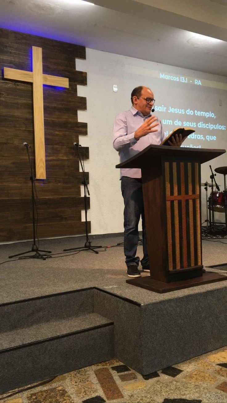 a man standing at a podium in front of a projector screen with a cross on it