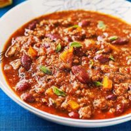 a white bowl filled with chili and meat on top of a blue table cloth next to bread