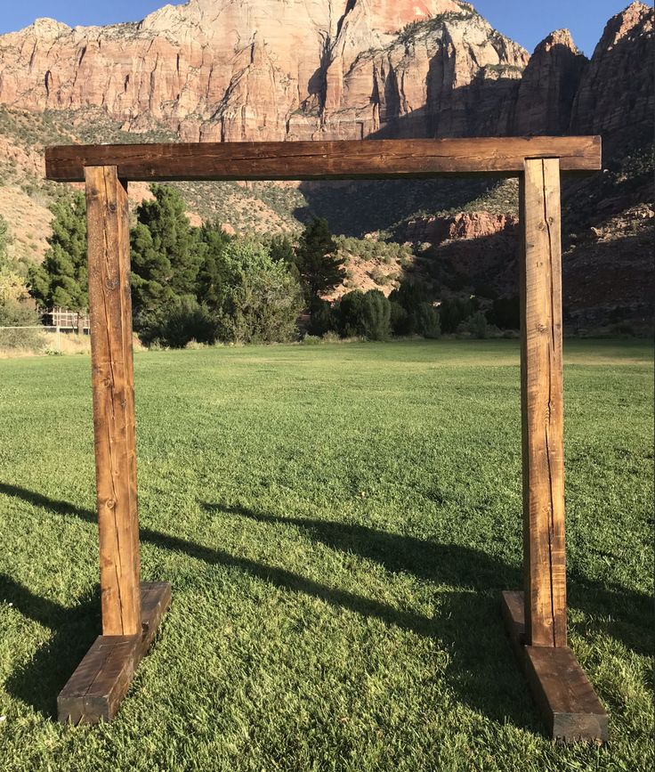 a wooden frame sitting on top of a lush green field next to a tall mountain