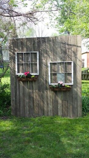 two windows on the side of a wooden building with flowers in each window and grass around them