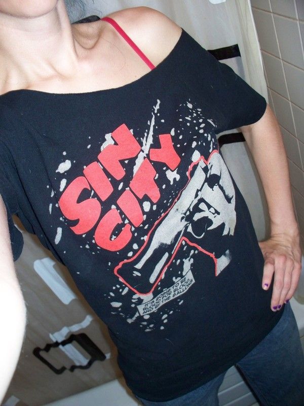 a woman standing in front of a bathroom mirror wearing a black shirt with red letters on it