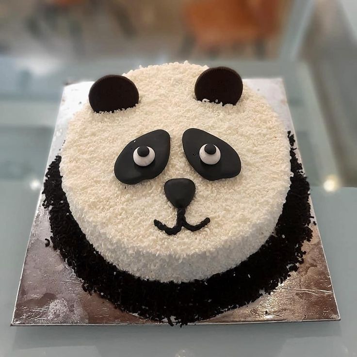 a panda bear cake with white frosting and black icing on a silver platter