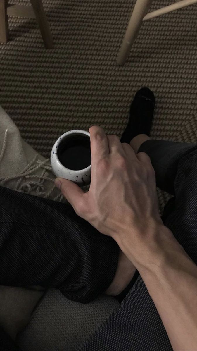 a person is holding a coffee cup in their hand while sitting on the floor next to a chair