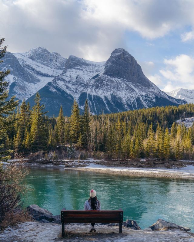 a person sitting on a bench in front of a mountain lake