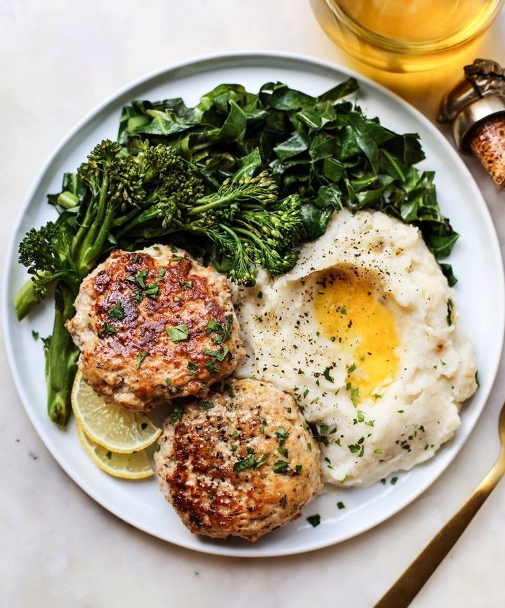 a white plate topped with meat patties and veggies next to a glass of orange juice