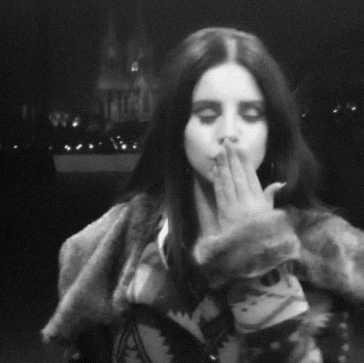 a woman in a fur coat covers her mouth with her hands as she stands outside at night