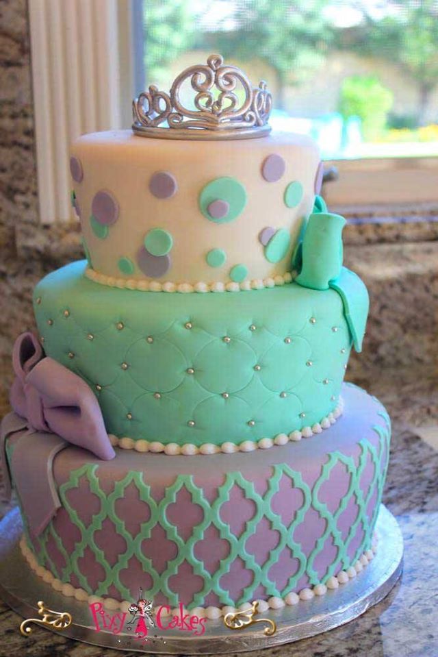 a three tiered cake with polka dots and a tiara on top, sitting in front of a window