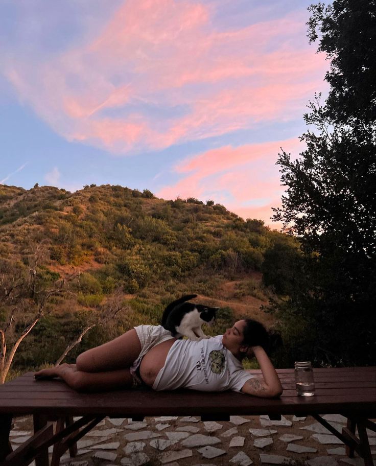 a woman laying on top of a wooden bench next to a black and white cat