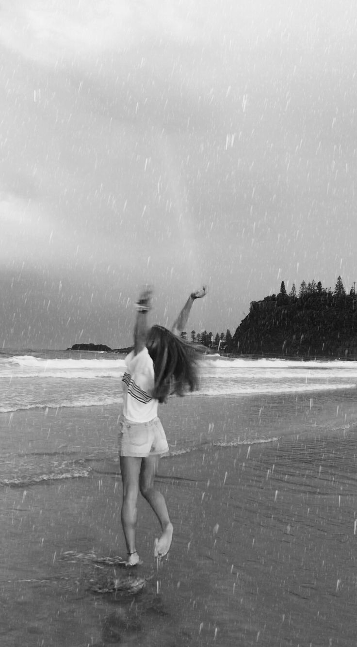 a woman standing on top of a beach next to the ocean under a cloudy sky