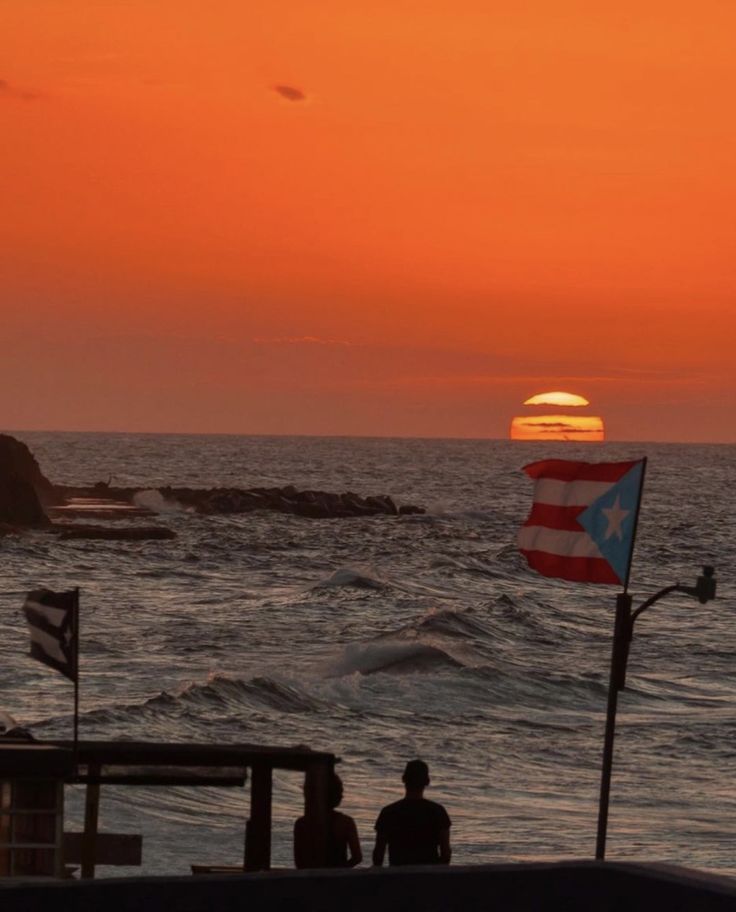 the sun is setting over the ocean and people are on the beach