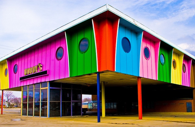 a multicolored building with round windows on the top and bottom floor, in front of a parking lot