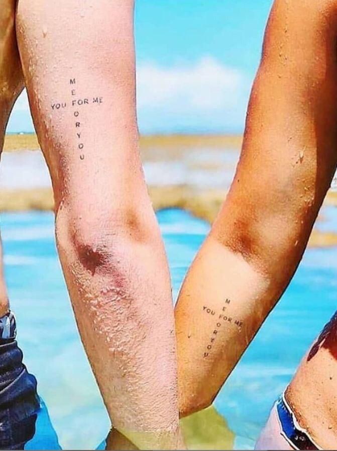 two people standing next to each other with tattoos on their legs and one is holding the other's leg