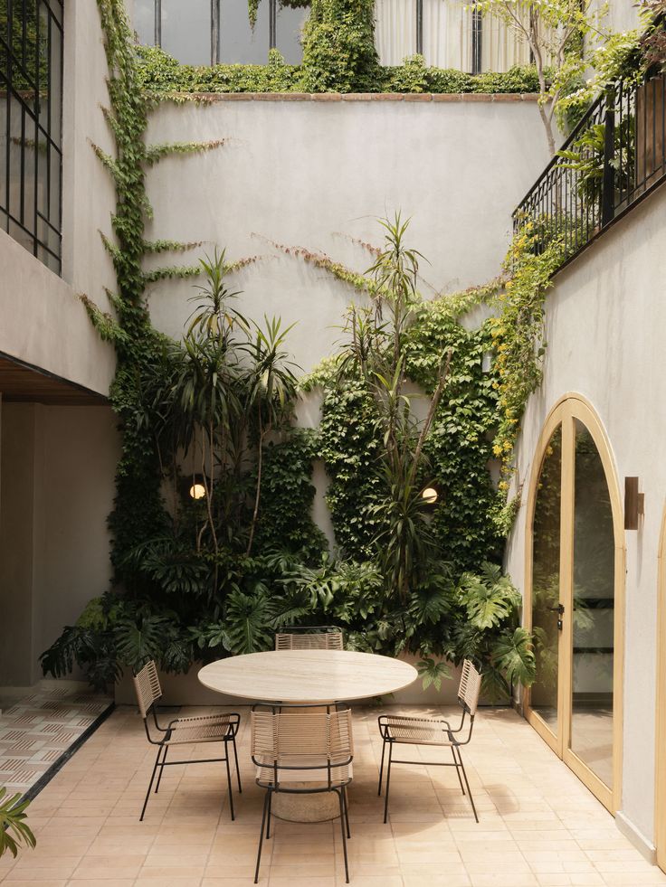 an outdoor dining table and chairs in front of a wall with plants growing on it