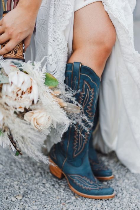 a woman in cowboy boots holding a bouquet of white flowers and feathers on the ground