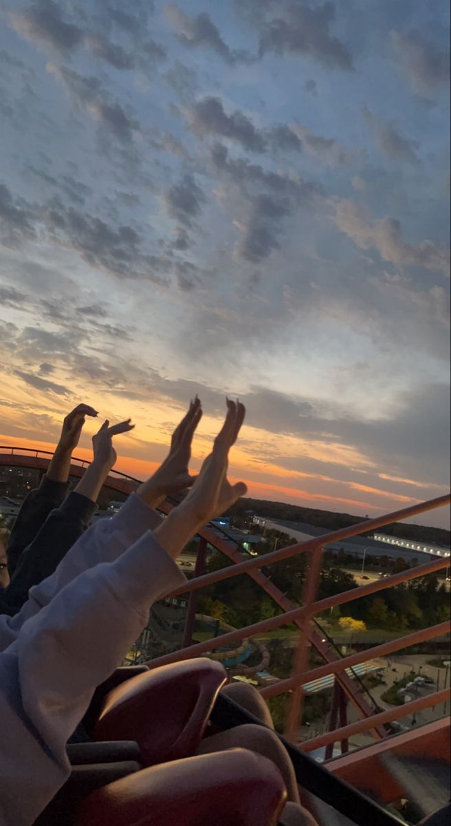 two people are sitting on a roller coaster at sunset with their hands in the air