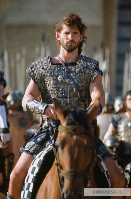 a man riding on the back of a brown horse next to other men in armor