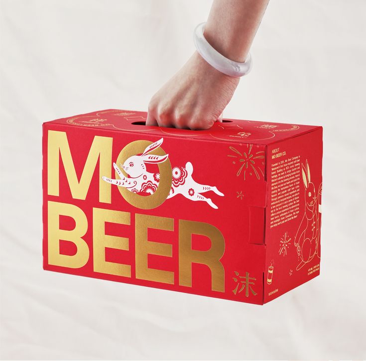 a person holding a red box with gold foil lettering on it that says mo beer