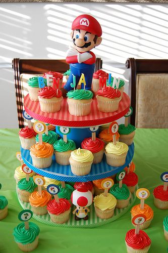 a mario birthday cake and cupcakes on a green tablecloth with other cupcakes