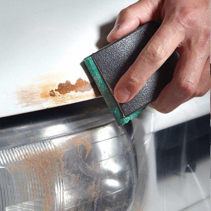 a person is cleaning the front bumper of a car with a sponge and a rag