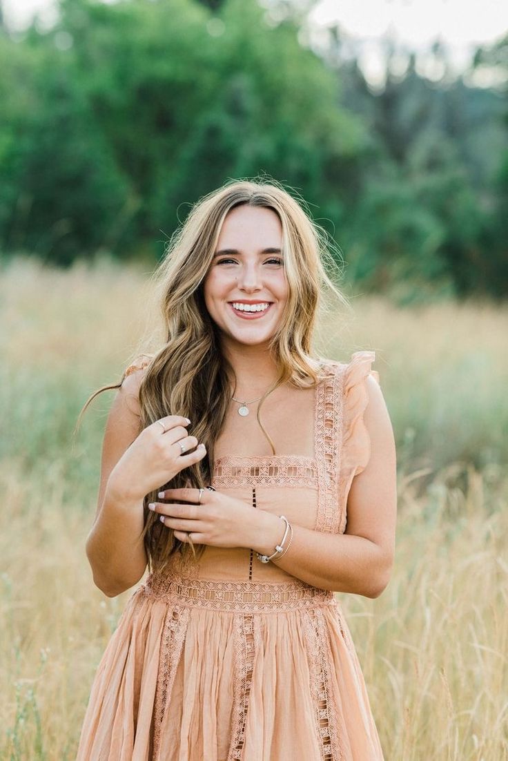 a woman standing in tall grass with her hands on her chest and smiling at the camera