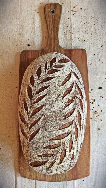 a wooden cutting board topped with a loaf of bread on top of a white table