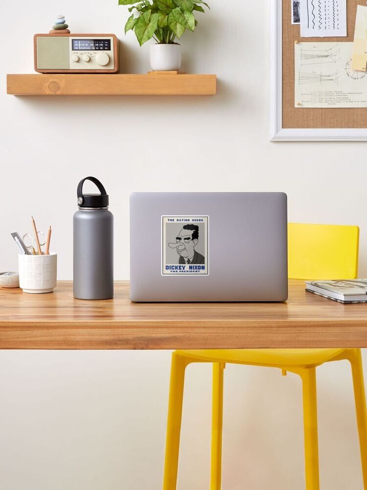 a laptop computer sitting on top of a wooden desk next to a yellow chair and potted plant