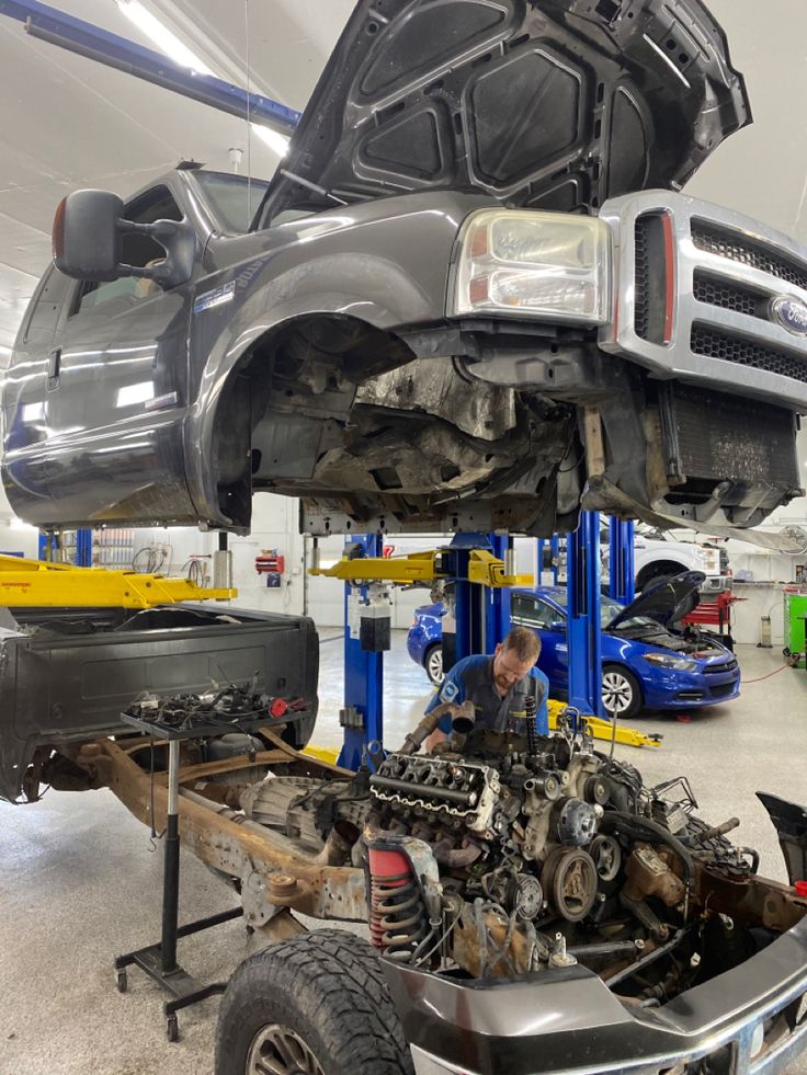 a car being worked on in a garage with two men working on the front bumpers