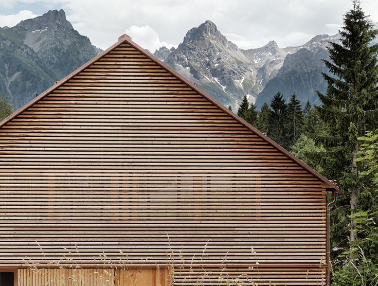 a large wooden building with mountains in the backgroung and trees around it