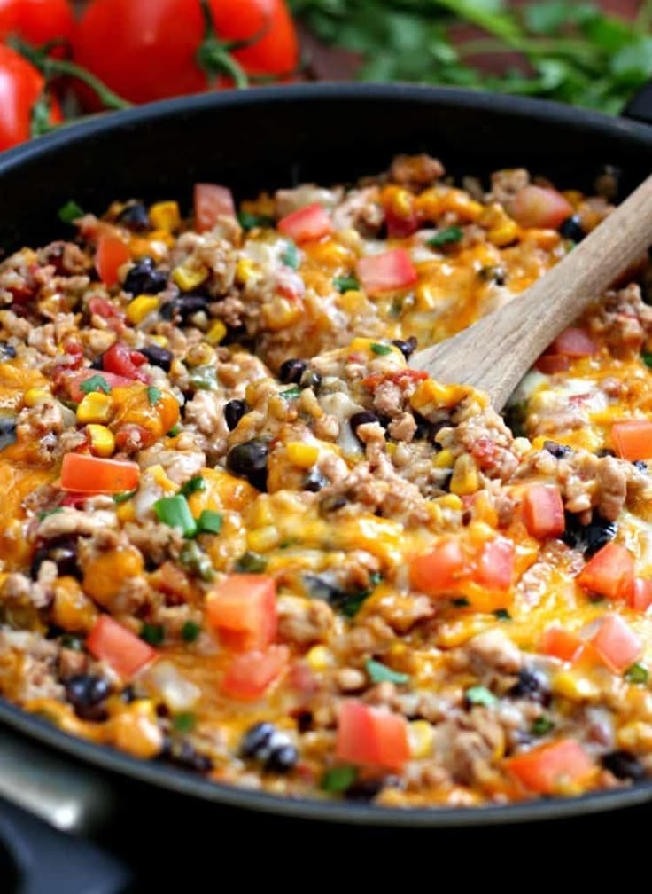 a skillet filled with taco salad and topped with a wooden spoon next to tomatoes