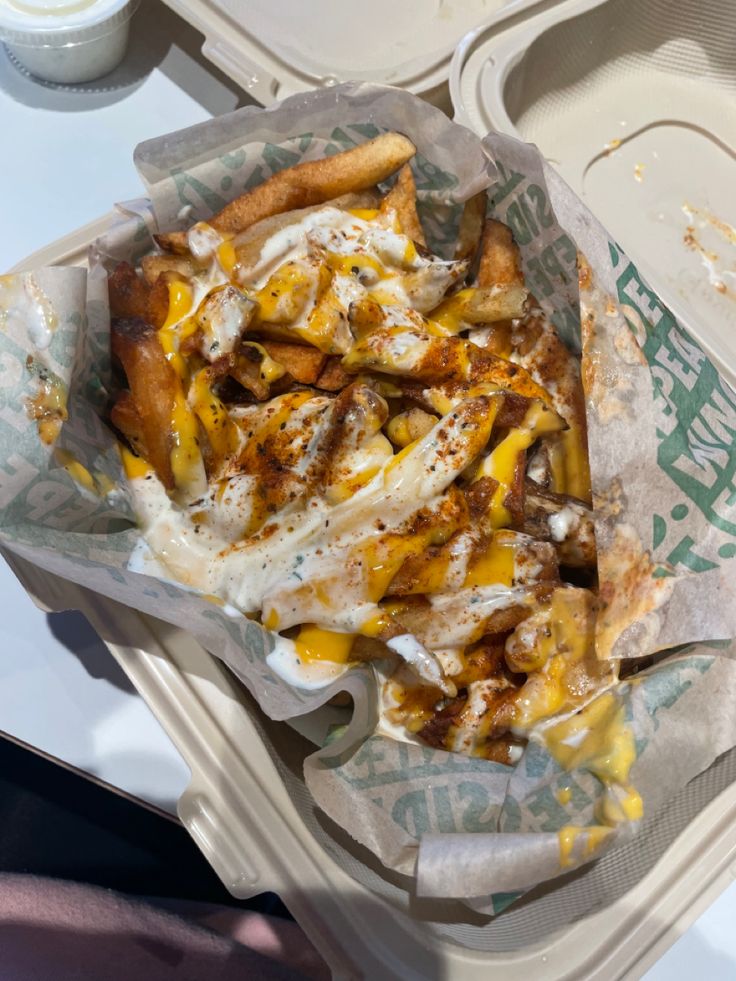 a container filled with french fries covered in cheese and other toppings on top of it