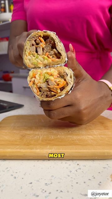 a woman holding two burritos on top of a wooden cutting board