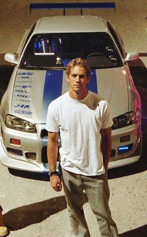 a man standing in front of a white car with blue stripes on it's hood